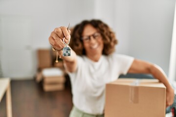 Middle age hispanic woman holding cardboard box and key of house at new home