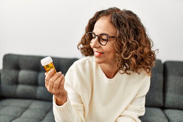 Middle age hispanic woman smiling confident holding pills at home