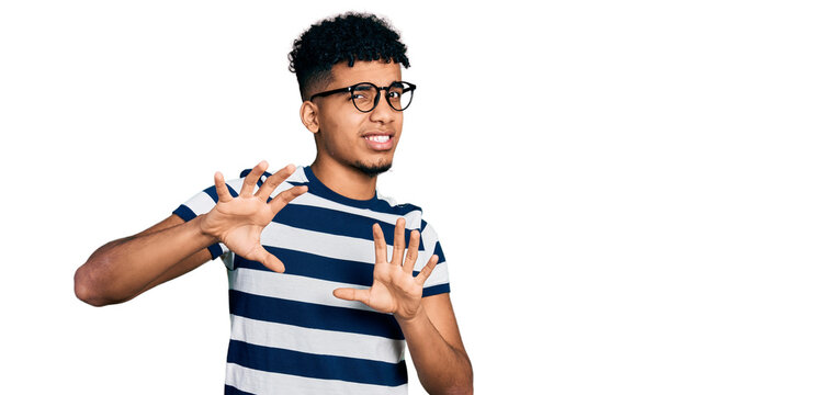 Young african american man wearing casual clothes and glasses disgusted expression, displeased and fearful doing disgust face because aversion reaction. with hands raised