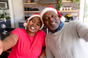 Happy african american senior couple taking selfie in kitchen at christmas time