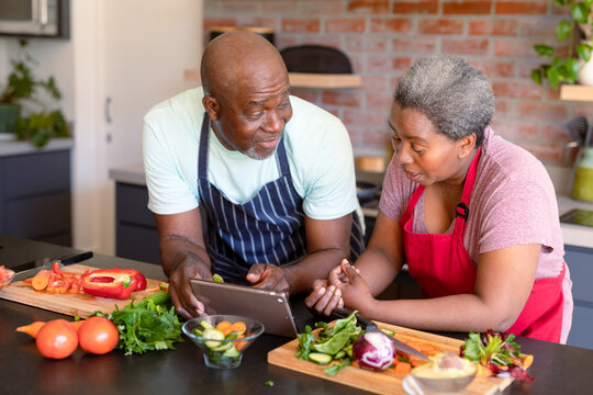 Happy african american senior couple cooking together in kitchen, using tablet - Powered by Adobe