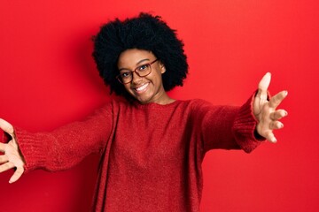 Fototapeta na wymiar Young african american woman wearing casual clothes and glasses looking at the camera smiling with open arms for hug. cheerful expression embracing happiness.