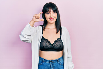 Young hispanic woman wearing lingerie smiling and confident gesturing with hand doing small size sign with fingers looking and the camera. measure concept.