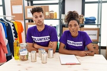 Young interracial people wearing volunteer t shirt at donations stand afraid and shocked with surprise expression, fear and excited face.