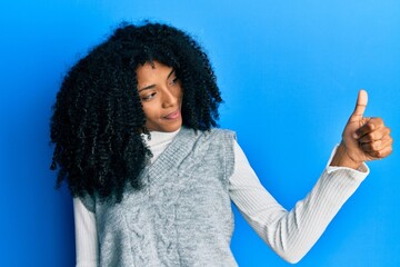 African american woman with afro hair wearing casual winter sweater looking proud, smiling doing thumbs up gesture to the side