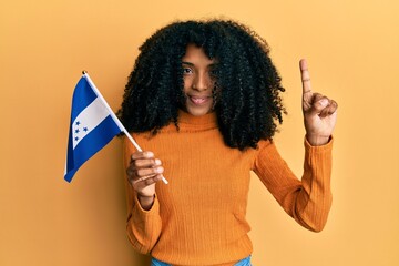 African american woman with afro hair holding honduras flag smiling with an idea or question...