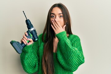 Young hispanic girl holding screwdriver covering mouth with hand, shocked and afraid for mistake....