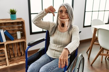 Middle age grey-haired woman sitting on wheelchair with collar at home with angry face, negative...