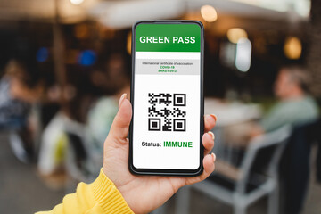 Immune digital green pass certificate for coronavirus vaccine with bar restaurant on background - Focus on woman hand holding mobile phone