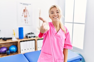 Young caucasian woman working at pain recovery clinic smiling friendly offering handshake as greeting and welcoming. successful business.