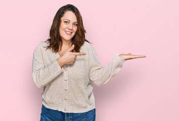 Young plus size woman wearing casual clothes amazed and smiling to the camera while presenting with hand and pointing with finger.