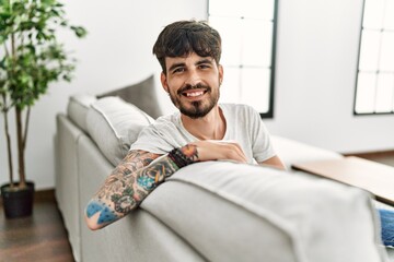 Young hispanic man smiling confident sitting on the sofa at home