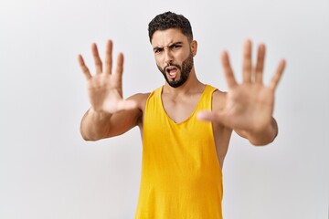 Young handsome man with beard standing over isolated background afraid and terrified with fear expression stop gesture with hands, shouting in shock. panic concept.