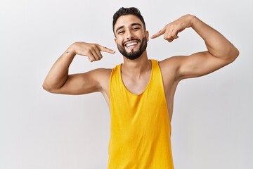 Young handsome man with beard standing over isolated background smiling cheerful showing and pointing with fingers teeth and mouth. dental health concept.