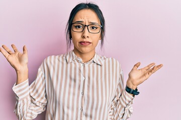 Young hispanic girl wearing casual clothes and glasses clueless and confused with open arms, no idea and doubtful face.