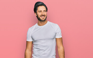 Obraz premium Young hispanic man wearing casual white t shirt looking away to side with smile on face, natural expression. laughing confident.