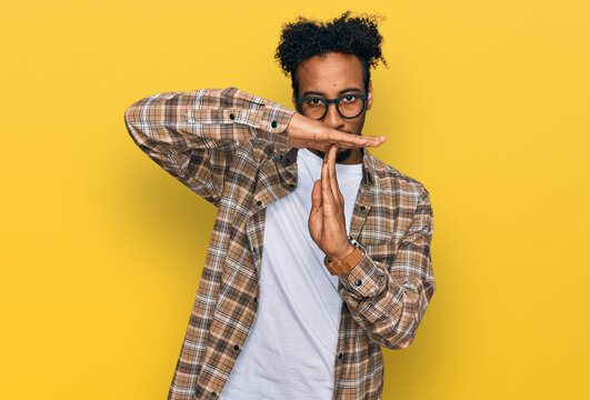 Young african american man with beard wearing casual clothes and glasses doing time out gesture with hands, frustrated and serious face
