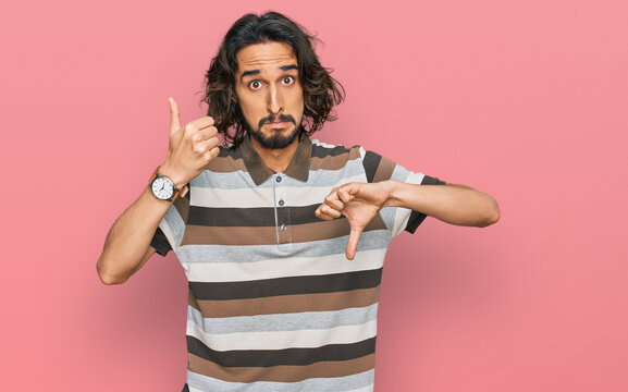 Young hispanic man wearing casual clothes doing thumbs up and down, disagreement and agreement expression. crazy conflict