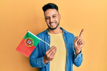 Young arab man holding portugal flag smiling happy pointing with hand and finger to the side