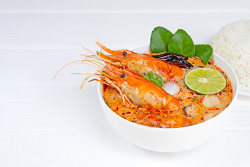 Tom Yum Goong or Shrimp soup spicy sour Soup Traditional food in Thailand contains chili, lime, ginger, galangal, lemongrass, lime leaf,  white wood background.