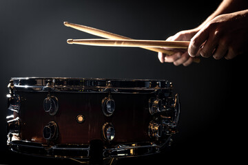 Snare drum and drummer's hands hitting drumsticks against a dark background.