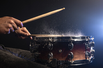 A man plays with drumsticks on a snare drum with splashing water.