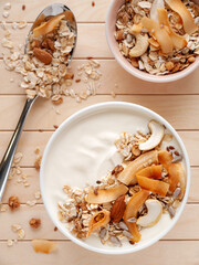 Bowl of yogurt with muesli, oatmeal, nuts and coconut chips on wooden background