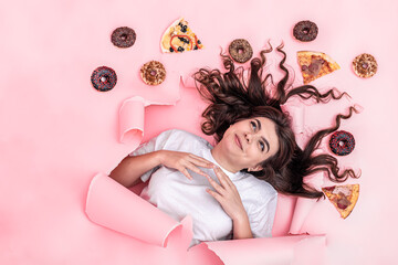 Obraz na płótnie Canvas Attractive young woman on a pink background with pizza and donuts, top view.
