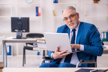 Old male employee in wheel-chair sitting in the office
