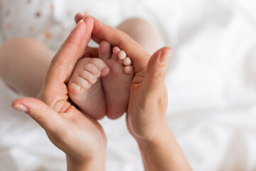 Obraz na płótnie Canvas closeup of the bare feet of a newborn baby in his mother's hands on a white background. top view. caring for a newborn. mother's love. space for text. High quality photo