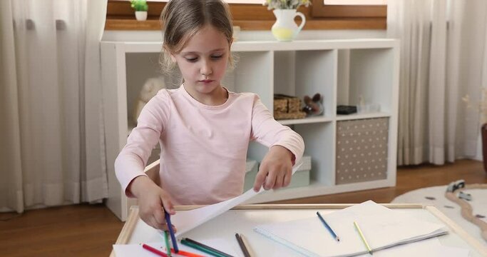 Cute little artist. Focused small girl enjoy drawing in album using crayons at cozy child room childcare setting. Smart little schoolgirl spend time at table create fantasy picture enjoy making sketch