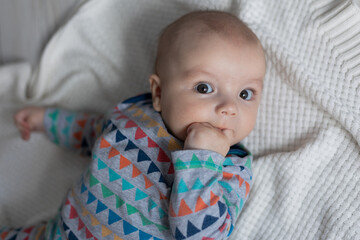 portrait of a newborn baby in a colored bodysuit lying on his back on a knitted white blanket made of natural cotton. top view. space for text. High quality photo