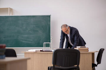 Old male teacher in front of blackboard