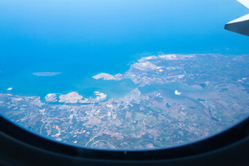 A view through the window of an airplane that sees the city, the fields, the sea and the clouds.