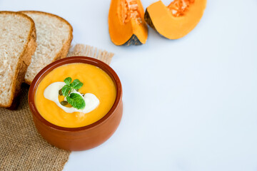 yellow pumpkin soup served and ready with bread, two pieces of raw pumkin in the background, thanksgiving or winter meal, traditional autumn food. 