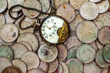 A bunch of old silver coins with a broken pocket watch on top