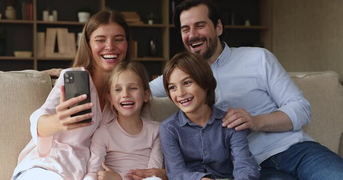Family picture. Cheerful bonding family young mom dad preteen children siblings daughter son sit close together on cozy couch posing for selfie on smartphone. Joyful couple with kids make video call