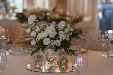 White tablecloths with clear vases and white flowers and fern arrangements. Golden colored plates, peavh napkins, table numbers and mirror centerpieces.