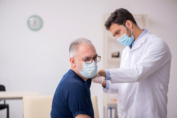 Obraz premium Old male patient visiting young male doctor in vaccination conce