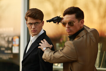 Model man with sunglasses and holding a gun in hand holding hostage onever businessman.