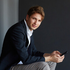 Portrait of a handsome young businessman in elegant suit holding a cell phone, over black background.