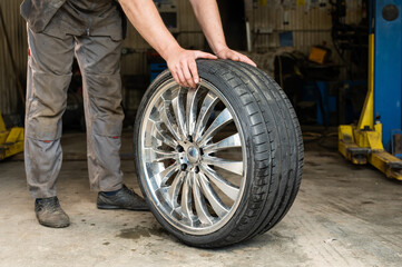Obraz premium An auto mechanic holds a wheel of a car. Change of car tires according to the season