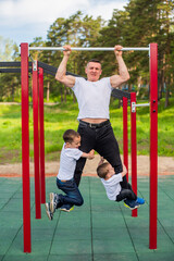 Obraz premium Caucasian man and two boys doing exercises outdoors. The father pulls himself up on the horizontal bar with his sons on the playground.