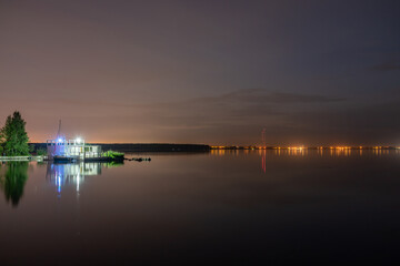 Fototapeta premium Evening forest on the lake shore with moored yacht at the edge of the city. Beautiful lake in the city park. Night park with lake in the city.