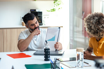 Mid adult indian boss man in the office showing coworkers market tendencies graph. Copy space.