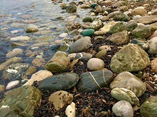 Stone beach view. Small stones along clear sea water. Beautiful sea coast tropical background texture.