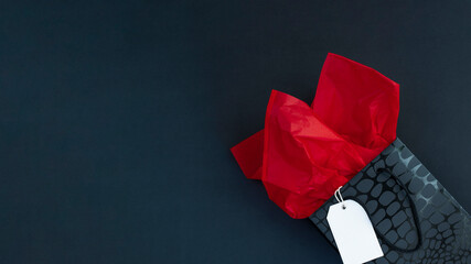 Black gift bag with red tissue paper and white label on black background