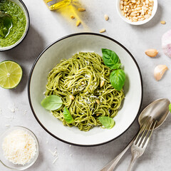 Pasta spaghetti with pesto sauce and fresh basil leaves in grey bowl. Light grey background. Top view.