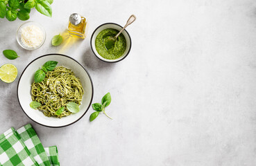 Pasta spaghetti with pesto sauce and fresh basil leaves in grey bowl. Light grey background. Top view.