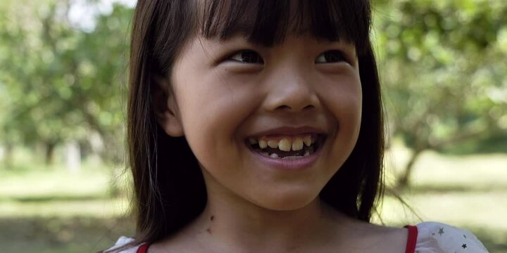 Portrait of little asian girl smiling looking happy. child having fun in park outdoors enjoying. 4k footage